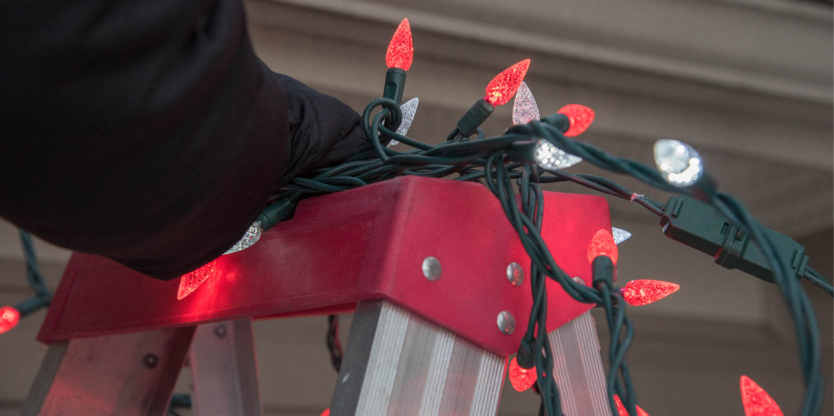 person on ladder installing holiday lights on gutter